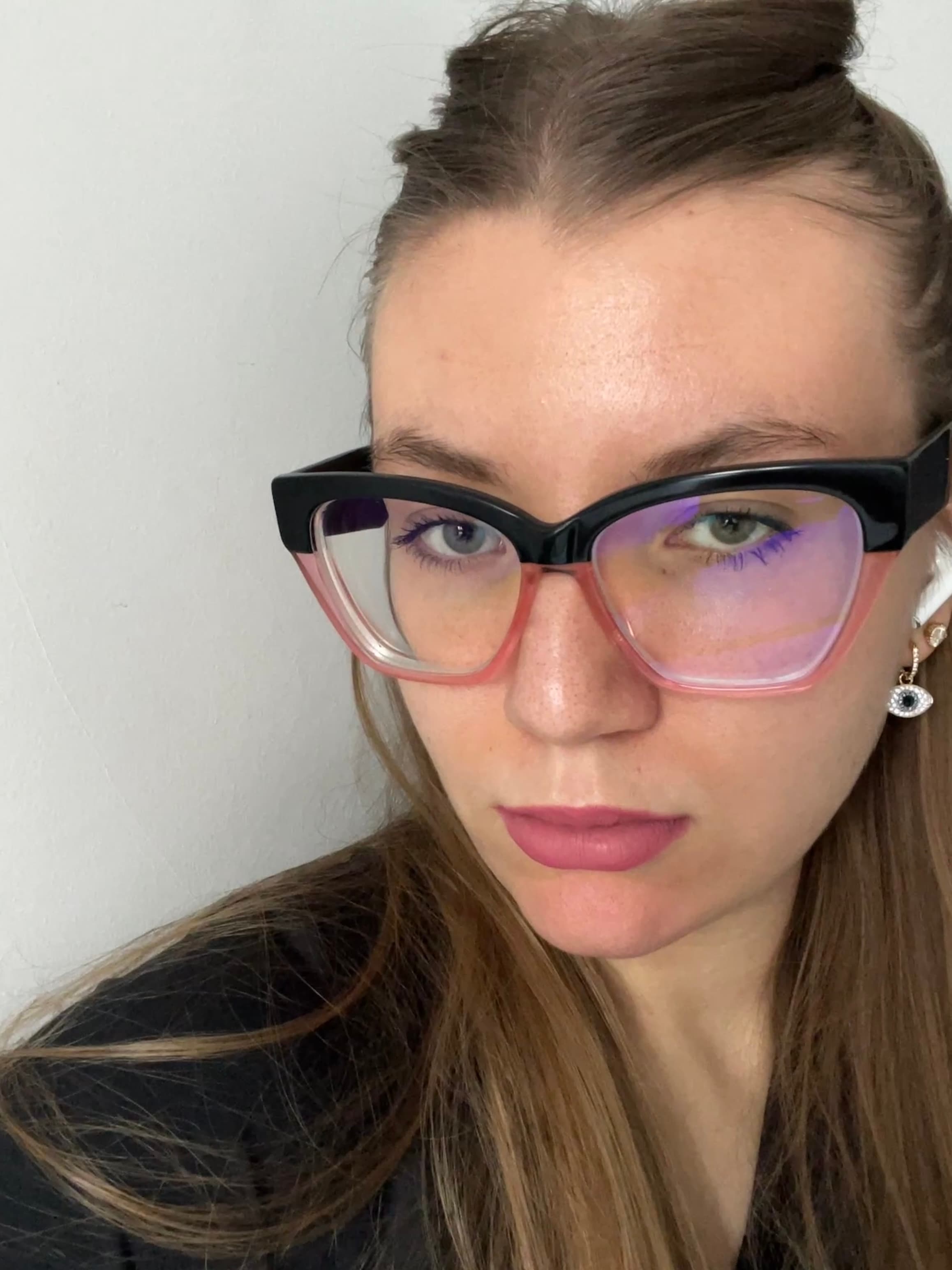 Donna con capelli castani, occhiali a gatta neri e rosa, rossetto rosa e sguardo serio.